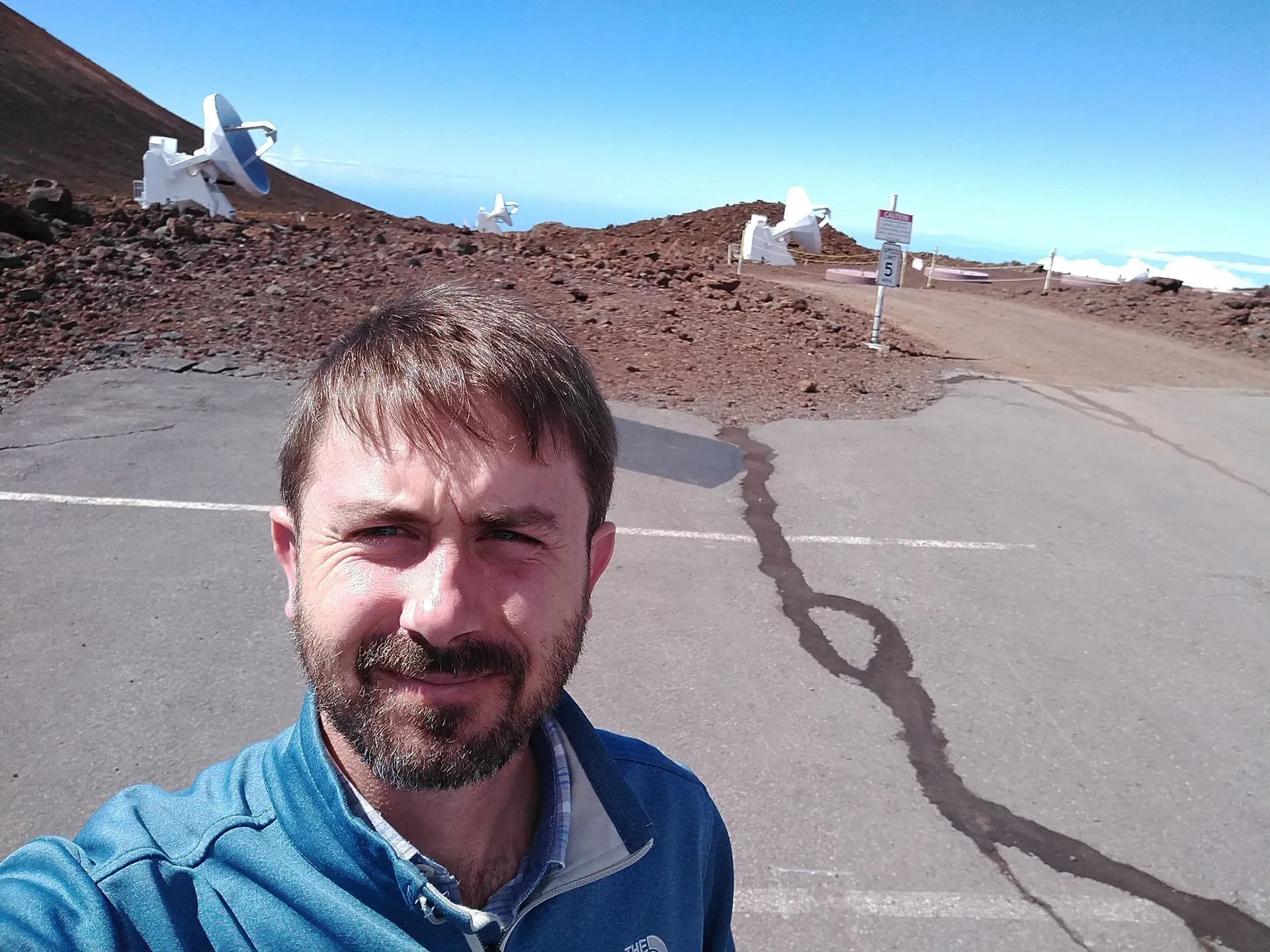 Chris Moriarty on the summit of Maunakea, with Submillimeter Array antennas behind him